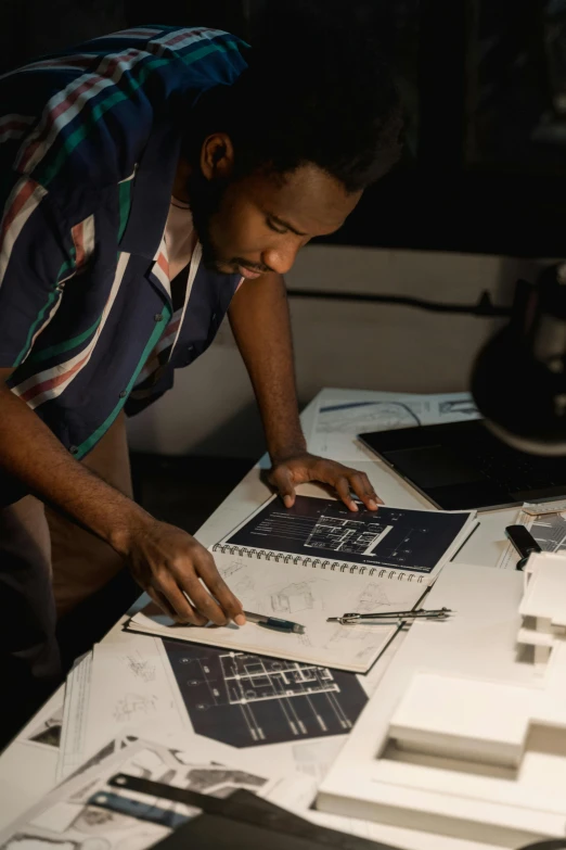 a man working on a project at a table, a silk screen, inspired by Afewerk Tekle, trending on unsplash, afrofuturism, nasa archives, mid night, blueprint, detailed color scan”