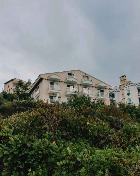 a building sitting on top of a lush green hillside, a portrait, by Elsa Bleda, unsplash, seaside victorian building, low quality photo, multiple stories, nice slight overcast weather