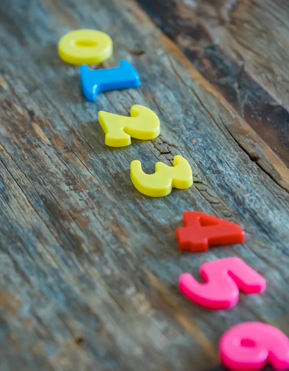 a wooden table topped with colorful plastic numbers, by Helen Stevenson, unsplash, letterism, high angle close up shot, detailed product image, multiple stories, close up shot from the side