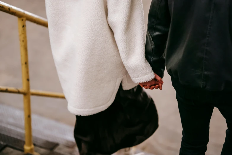 a man and a woman walking down a street holding hands, by Emma Andijewska, trending on pexels, happening, white jacket, close up details, soft and fluffy, wearing leather coat