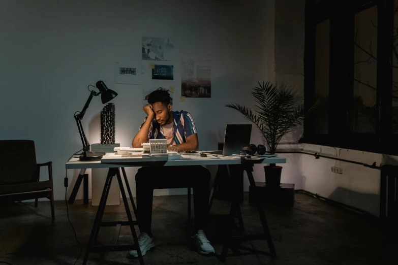 a man sitting at a desk in front of a laptop computer, pexels contest winner, arbeitsrat für kunst, lights off, afro tech, sleepy, backrooms office space