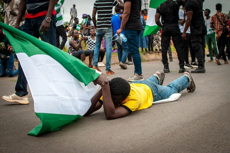 a man laying on the ground holding a flag, a photo, by Chinwe Chukwuogo-Roy, trending on pexels, happening, fuming effigy, green and white, 15081959 21121991 01012000 4k, leaking