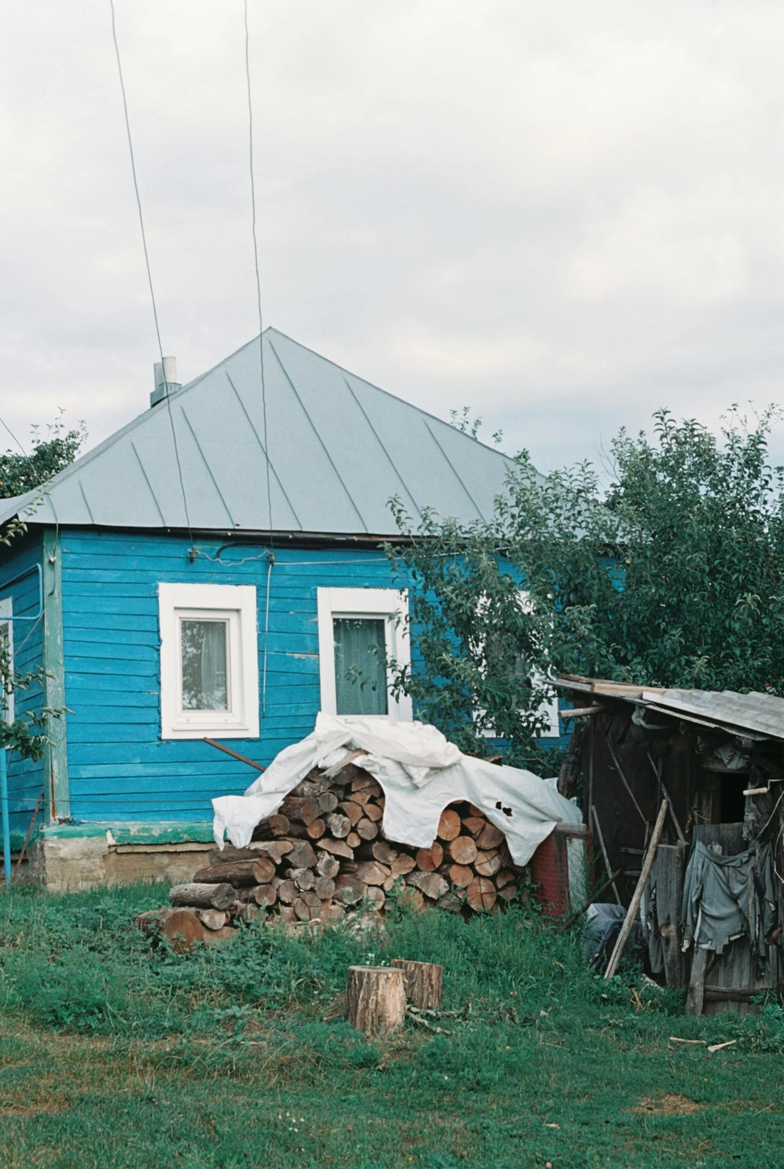 a blue house sitting on top of a lush green field, an album cover, inspired by Isaac Levitan, unsplash, soviet yard, wooden logs, 2000s photo, low quality footage