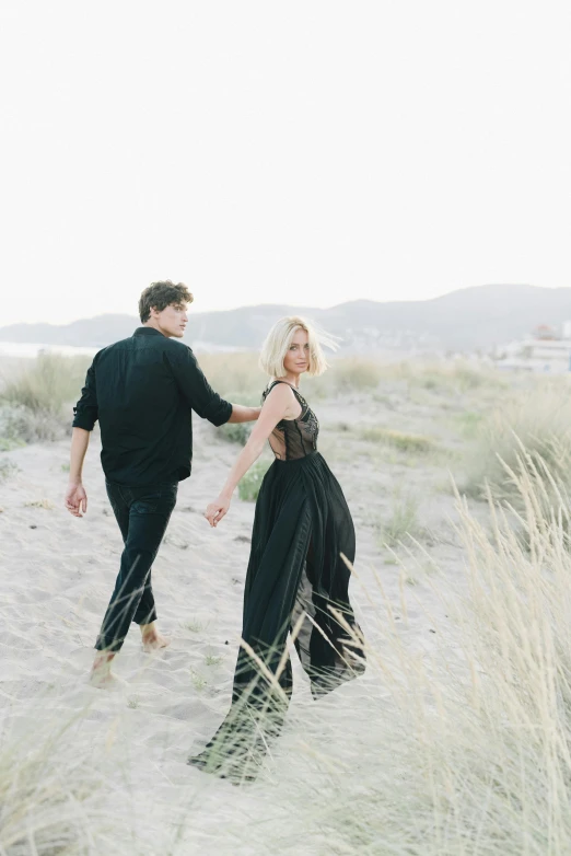 a man and woman walking on a beach holding hands, unsplash, renaissance, casual black clothing, standing in tall grass, charcoal and champagne, handsome girl