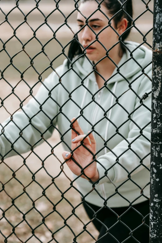 a woman standing in front of a chain link fence, inspired by Elsa Bleda, trending on pexels, gray hoodie, hand gesture, sports photo, 15081959 21121991 01012000 4k