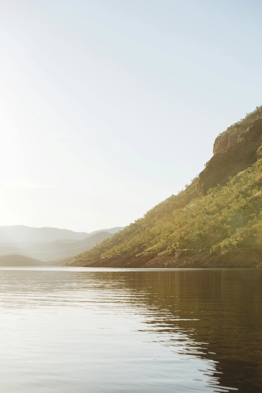 a large body of water with a mountain in the background, inspired by Johan Christian Dahl, trending on unsplash, sunlit landscape, in muted colours, ship on lake, canyon