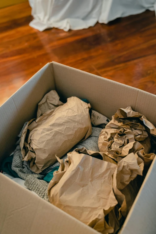 a box filled with clothes sitting on top of a wooden floor, brown paper, clay material, packaging, damaged