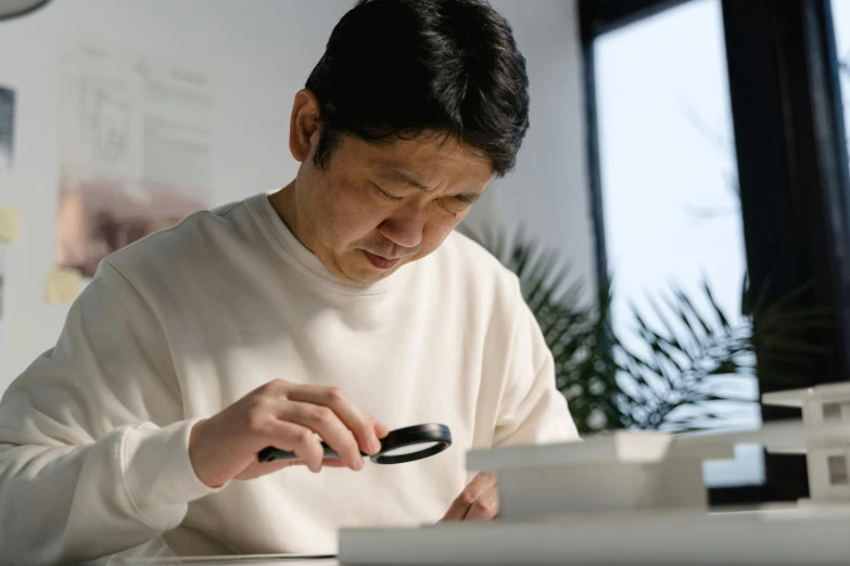 a man looking through a magnifying glass, inspired by Kanō Naizen, unsplash, shin hanga, on a white table, he is holding a smartphone, architect, japanese collection product