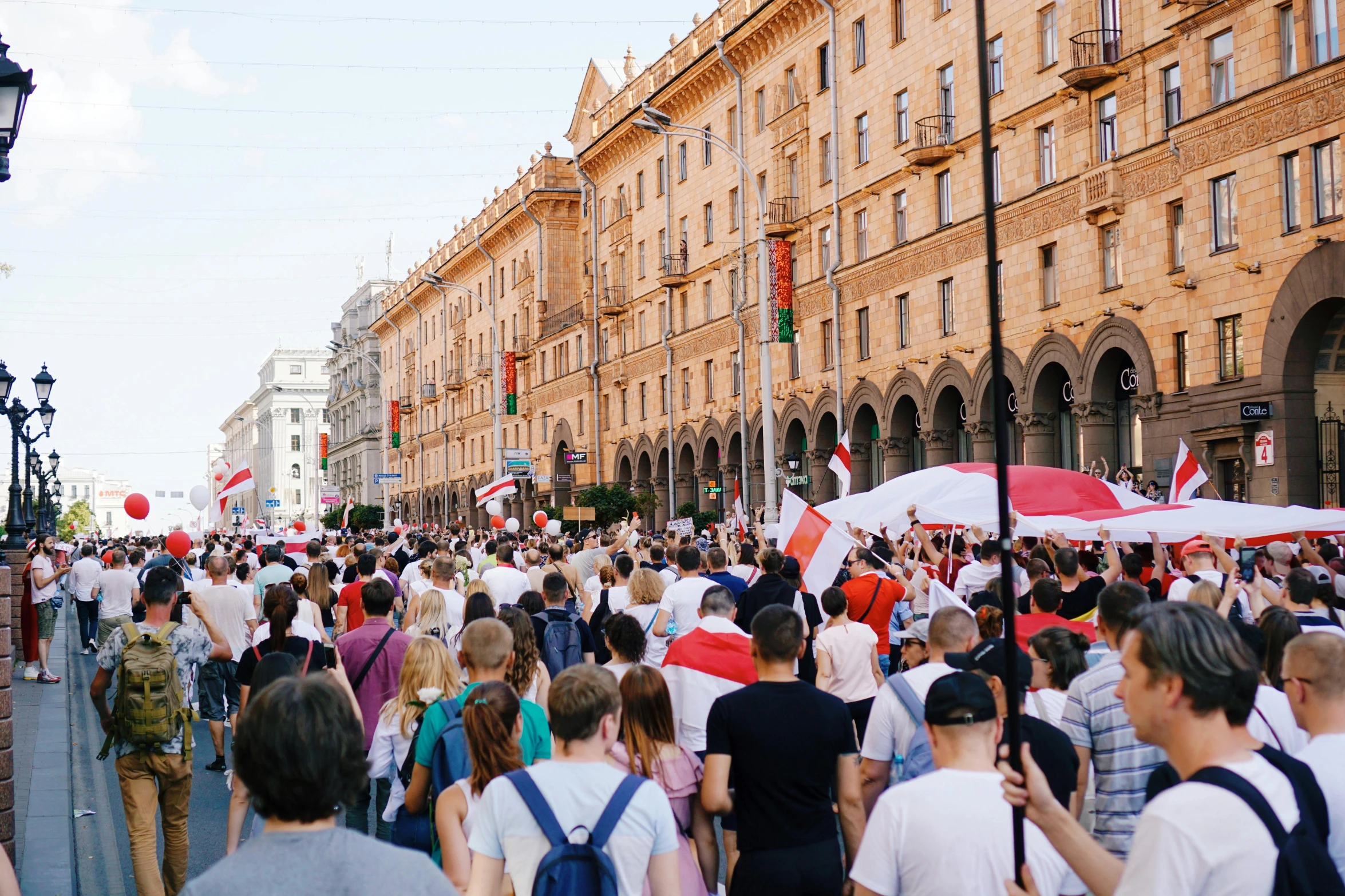 a crowd of people walking down a street next to tall buildings, a photo, by Julia Pishtar, pexels contest winner, socialist realism, president of belorussia, holding a white flag, italian, crowds panic