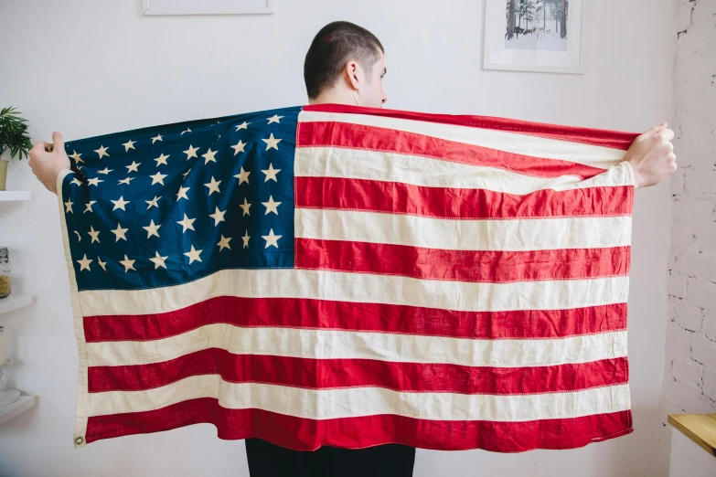 a man holding an american flag in his hands, an album cover, by Nina Hamnett, unsplash, pete davidson, state of the union, artisanal art, his cape is the american flag