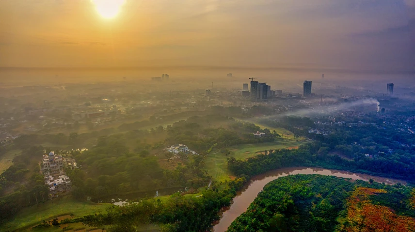 an aerial view of a city with a river running through it, a matte painting, pexels contest winner, sumatraism, hazy morning foggy, parks and public space, sri lankan landscape, sun setting