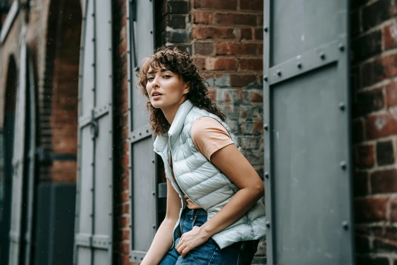 a woman leaning against a brick wall, by Nina Hamnett, trending on pexels, happening, wearing a vest, puffy, switch, alex heywood