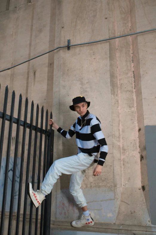 a man riding a skateboard up the side of a metal fence, an album cover, inspired by Horace Vernet, unsplash, striped sweater, he is wearing a hat, model posing, asher duran