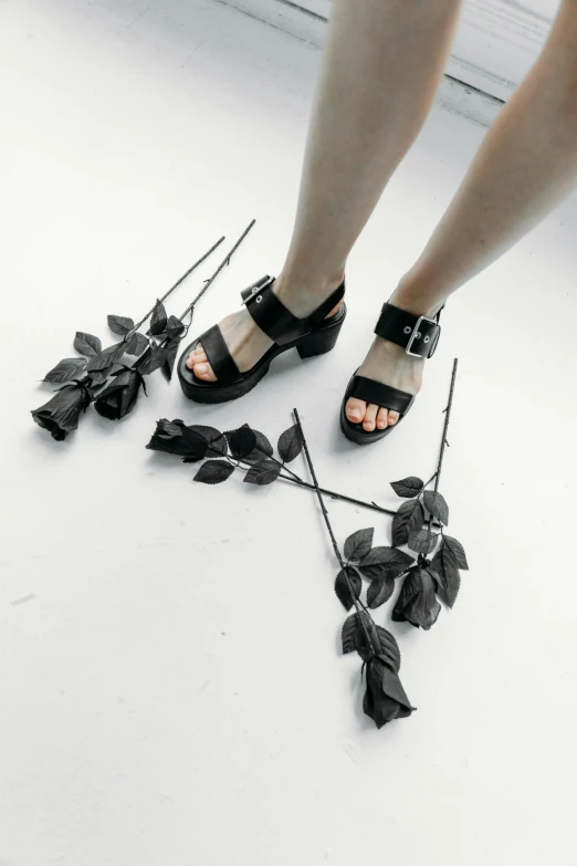 a woman standing on top of a white floor next to flowers, antipodeans, heavy metal rave shoes, black rose, collection product, sandals