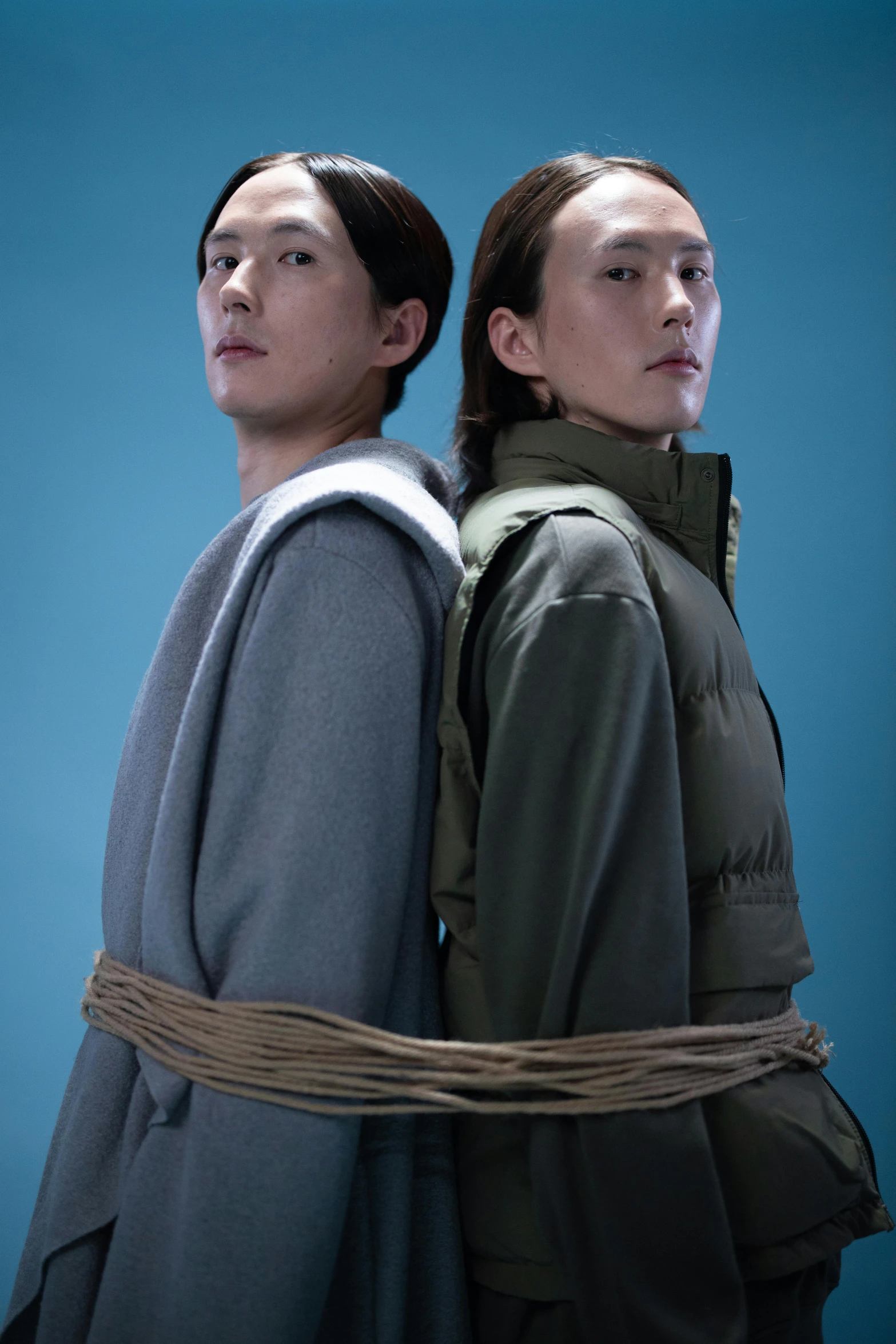 a couple of men standing next to each other, an album cover, inspired by Zhang Xiaogang, unsplash, conceptual art, wearing a turtleneck and jacket, with wires and bandages, arms behind back, showstudio