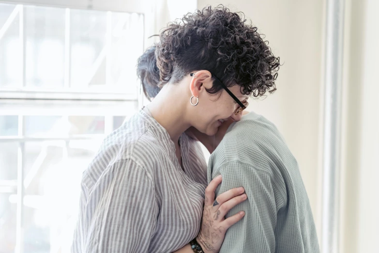 a woman hugging a man in front of a window, by Nina Hamnett, trending on pexels, antipodeans, lesbian, grieving, rebecca sugar, press photos