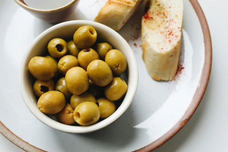 a bowl of olives and a piece of bread on a plate, unsplash, pickles, background image, glasgow, full body image