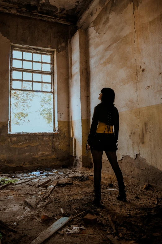 a woman standing in front of a window in an abandoned building, an album cover, pexels contest winner, back light, yellow walls, tourist photo, woman with black hair