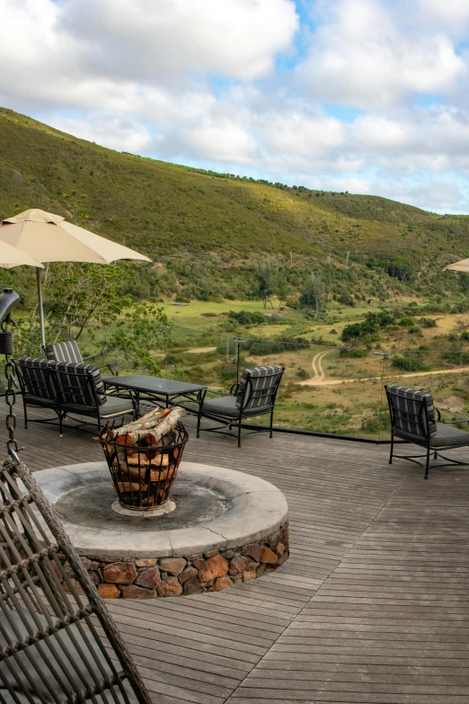 a group of chairs sitting on top of a wooden deck, green hills savanna tree, braziers, drinking, slate