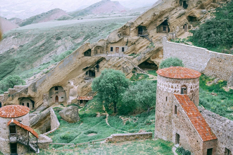 a couple of buildings sitting on top of a lush green hillside, by Muggur, renaissance, ancient caves, historical image, instagram photo, portra