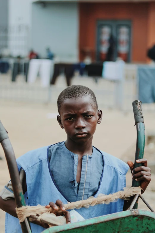 a man in a blue shirt holding a green wheelbarrow, by Matija Jama, pexels contest winner, in foreground boy with shotgun, yoruba body paint, holding two swords, teenage boy