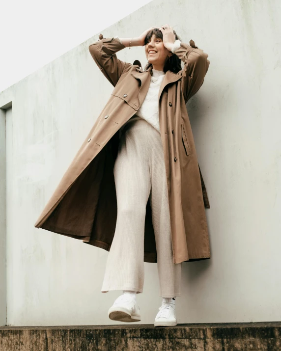 a woman in a trench coat leaning against a wall, trending on pexels, gradient brown to white, thumbnail, wearing human air force jumpsuit, product introduction photo