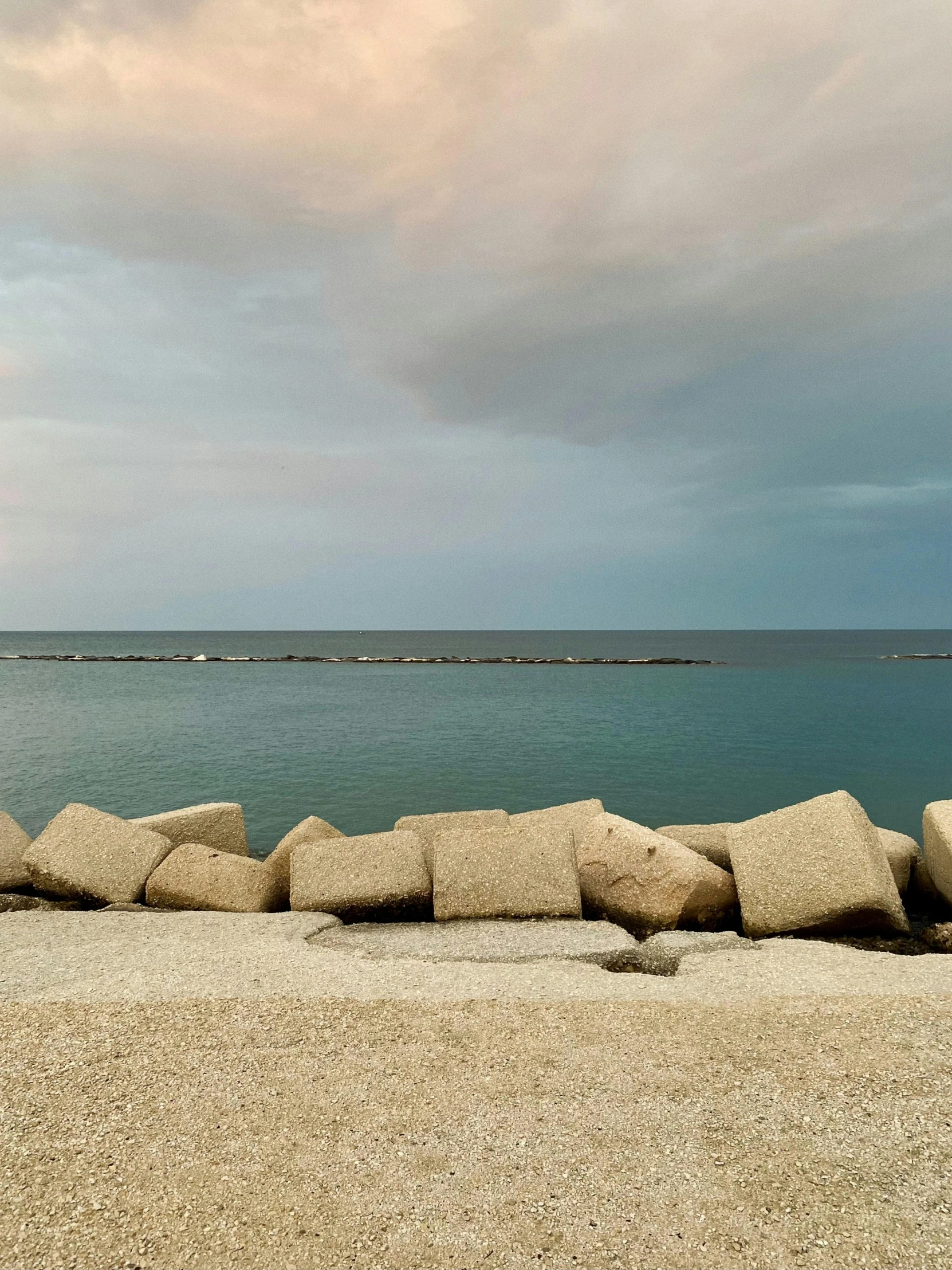 a group of rocks sitting on top of a beach next to the ocean, wall of water either side, urban surroundings, lorenzo lanfranconi, storm on horizon