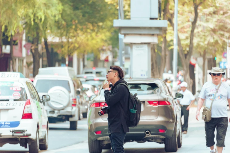 a man walking across a street while talking on a cell phone, by Nicolette Macnamara, pexels contest winner, happening, cover photo portrait of du juan, car traffic, square, paparazzi photo