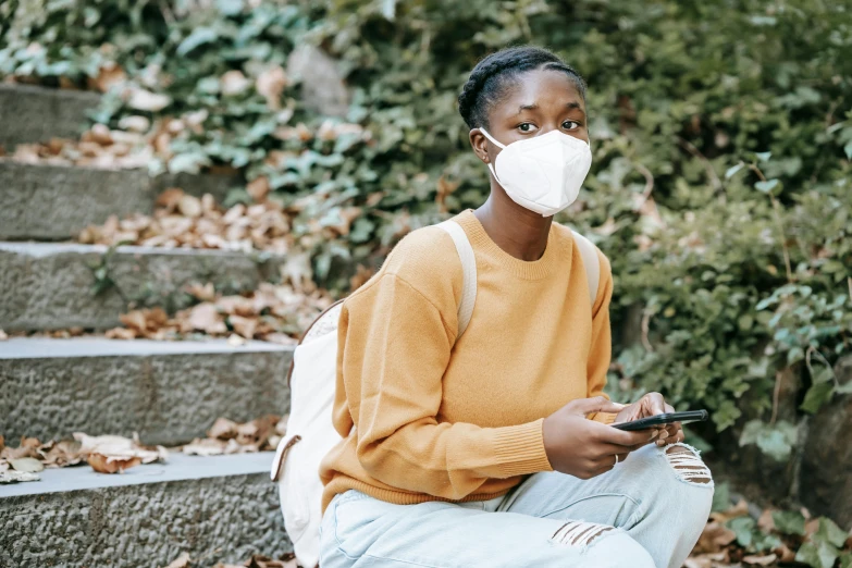 a woman wearing a face mask sitting on some steps, trending on pexels, brown skinned, respirator, realistic », student