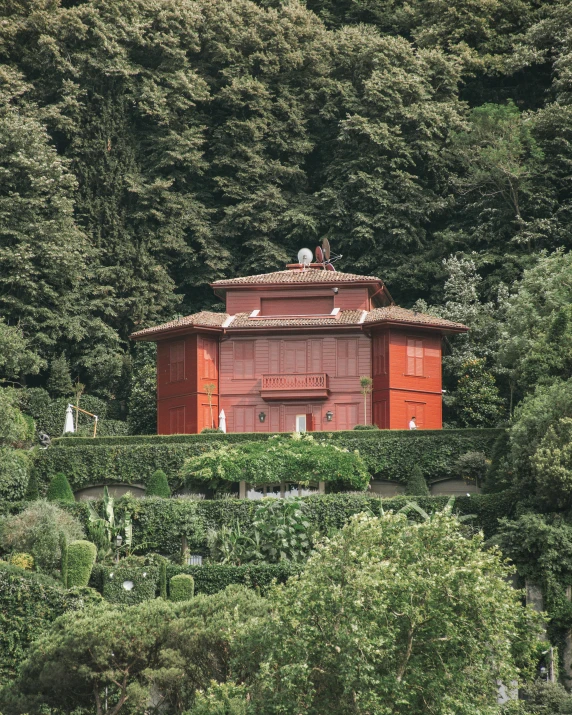 a red building sitting on top of a lush green hillside, inspired by Serafino De Tivoli, wooden banks, vouge italy, in the garden, shaved temple