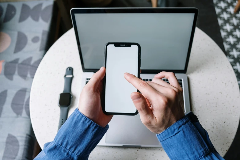 a person sitting at a table with a laptop and cell phone, a picture, by Dan Content, trending on pexels, corporate phone app icon, plain background, using a macbook, vertical orientation