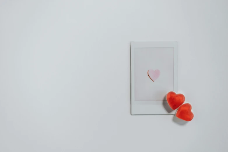a couple of red hearts sitting on top of a white table, a polaroid photo, by Emma Andijewska, trending on unsplash, miscellaneous objects, white and orange, standing in corner of room, product image