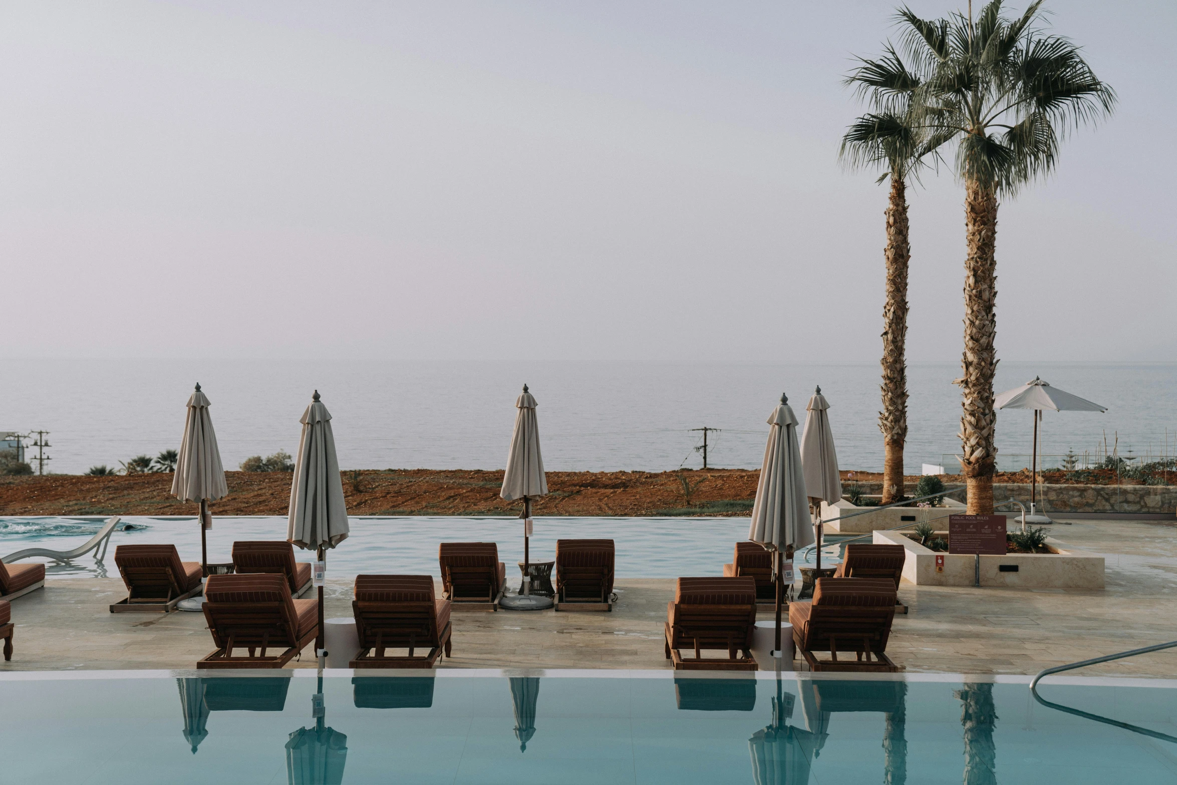 a group of lounge chairs sitting next to a swimming pool, pexels contest winner, les nabis, the dead sea, ocean view, muted brown, palm lines