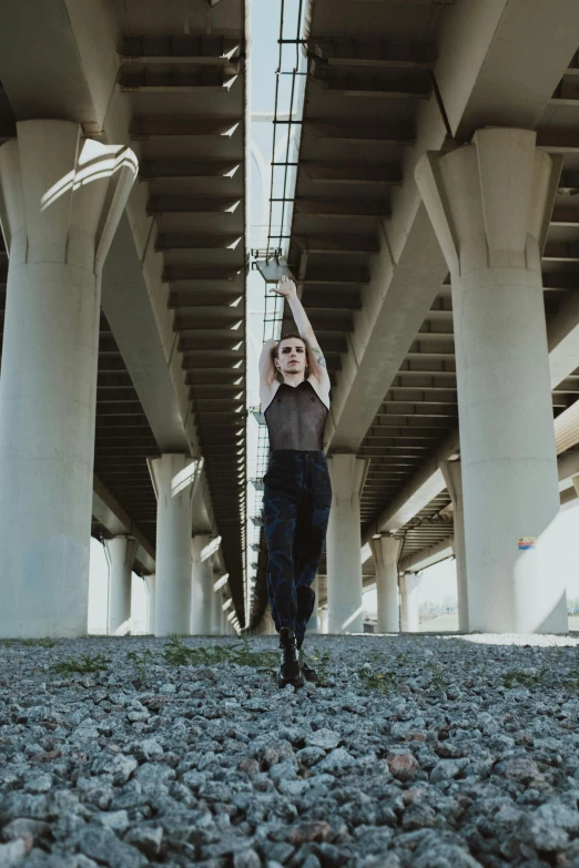 a woman standing under a bridge with her arms in the air, an album cover, inspired by Elizabeth Polunin, unsplash, an epic non - binary model, leather pants | natural lighting, on a parking lot, structure : kyle lambert