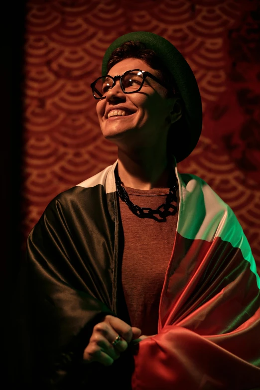 a man standing in front of a red wall, wearing a head scarf, betty la fea, under a spotlight, pride