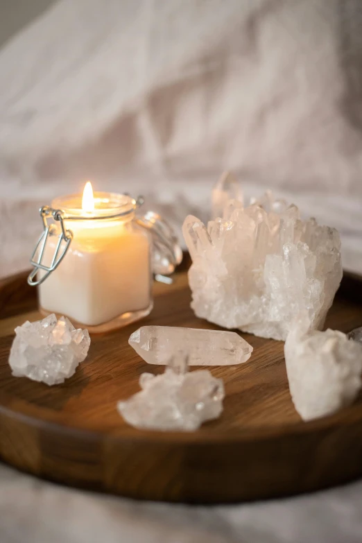 a candle sitting on top of a wooden tray, a still life, by Emily Mason, trending on pexels, organic crystals, whites, multiple lights, chiffon