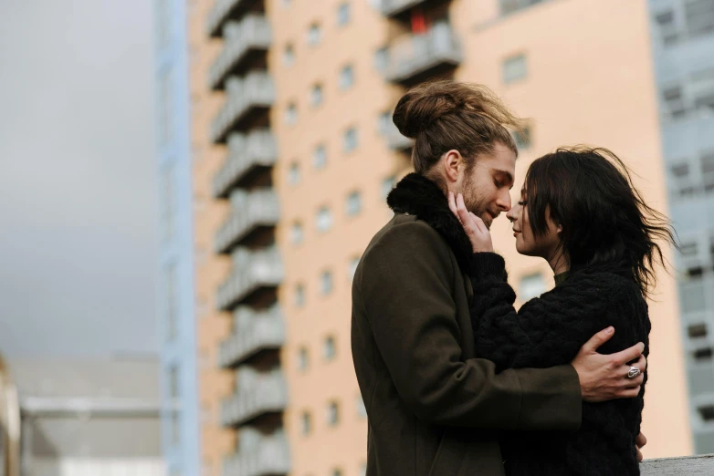 a couple standing next to each other in front of a tall building, by Emma Andijewska, pexels contest winner, happening, dreaming of kissing a girl, a cozy, hair, cutest