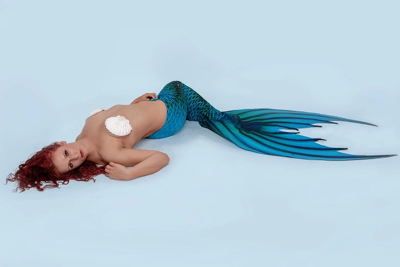 a woman in a mermaid costume laying on the ground, neoprene, blue scales with white spots, teal studio backdrop, back arched