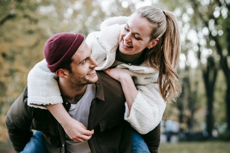a man carrying a woman on his back in a park, trending on pexels, beanie, playful smile, lachlan bailey, 15081959 21121991 01012000 4k
