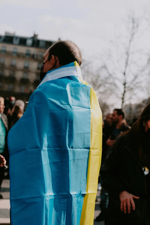 a man wrapped up in a blue and yellow blanket, trending on unsplash, symbolism, paris fashion week, russian opposition rally, slide show, square