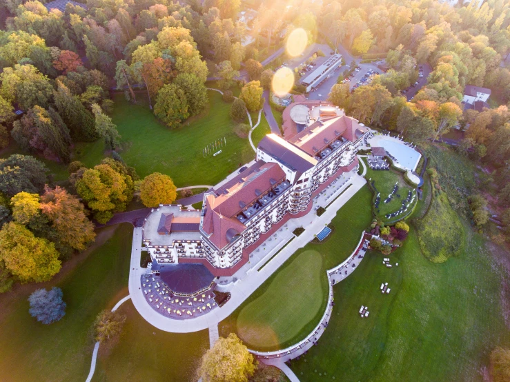 a large building sitting on top of a lush green field, art nouveau, sun lighting from above, resort, during autumn, lit from above