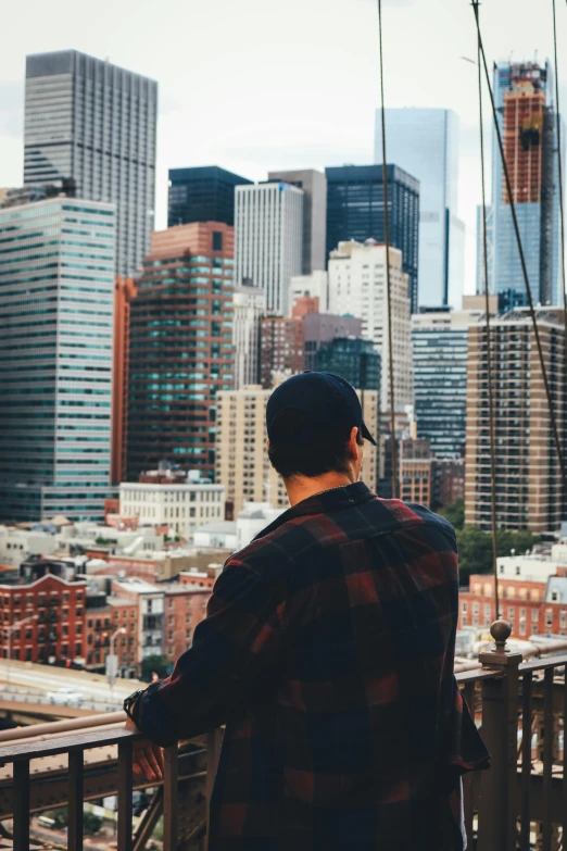 a man standing on top of a bridge looking at a city, new york buildings, influencer, wearing a backwards baseball cap, college