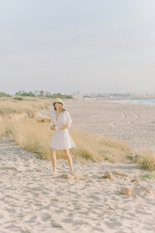 a woman standing on top of a sandy beach, inspired by Modest Urgell, unsplash, medium format. soft light, low quality photo, gif, lookbook