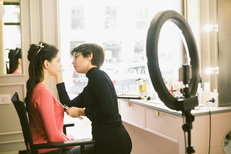 a woman getting her makeup done in front of a mirror, by Nina Hamnett, with backdrop of natural light, diane ramic, b - roll, commercial photo