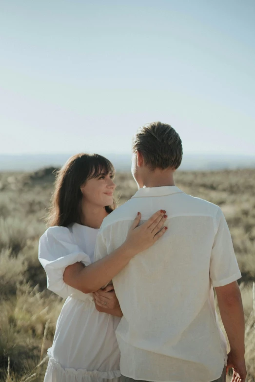 a man and woman standing next to each other in a field, unsplash, happening, wearing white clothes, desert setting, coast, tender