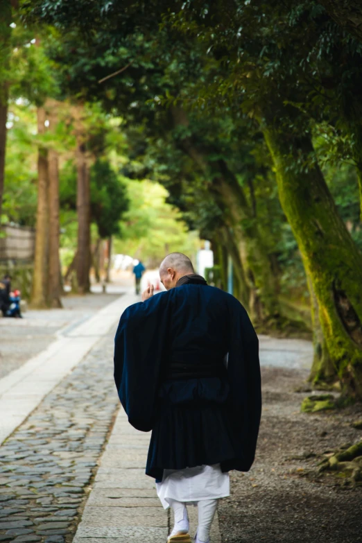 a man walking down a street while talking on a cell phone, a picture, inspired by Kanō Shōsenin, unsplash, blue robe, lush surroundings, head bowed slightly, an oldman