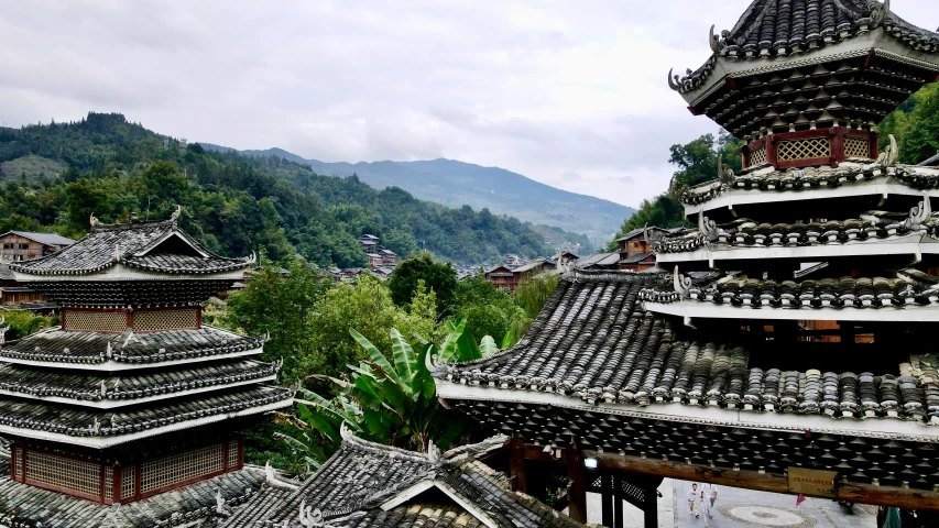 a group of buildings sitting on top of a lush green hillside, inspired by Gu An, peaked wooden roofs, china blue eyes, black, buildings carved out of stone