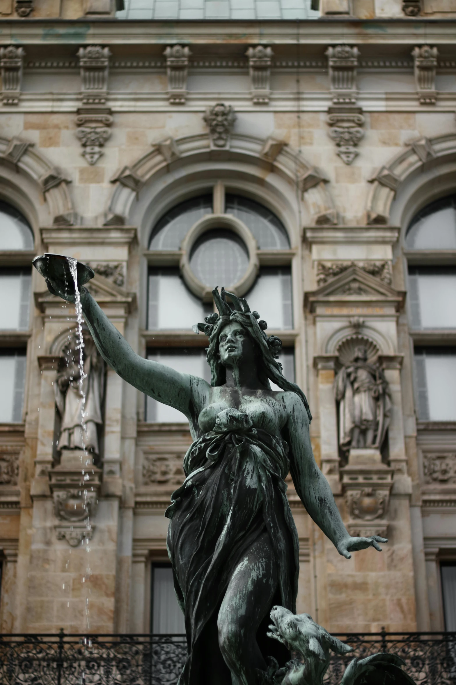a statue of a woman holding a bird in front of a building, by Joseph von Führich, fierce medusa, waving, fountain in the middle, brass semi - mechanical woman