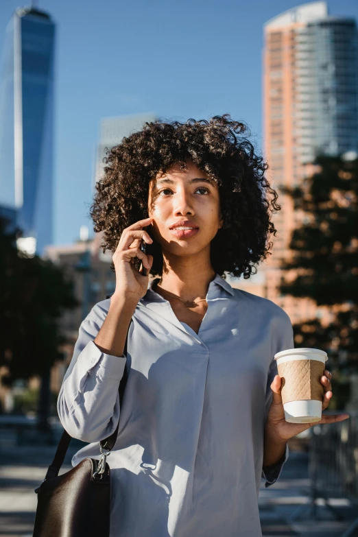 a woman talking on a cell phone while holding a cup of coffee, trending on pexels, happening, varying ethnicities, walking to work, curly haired, realistic »