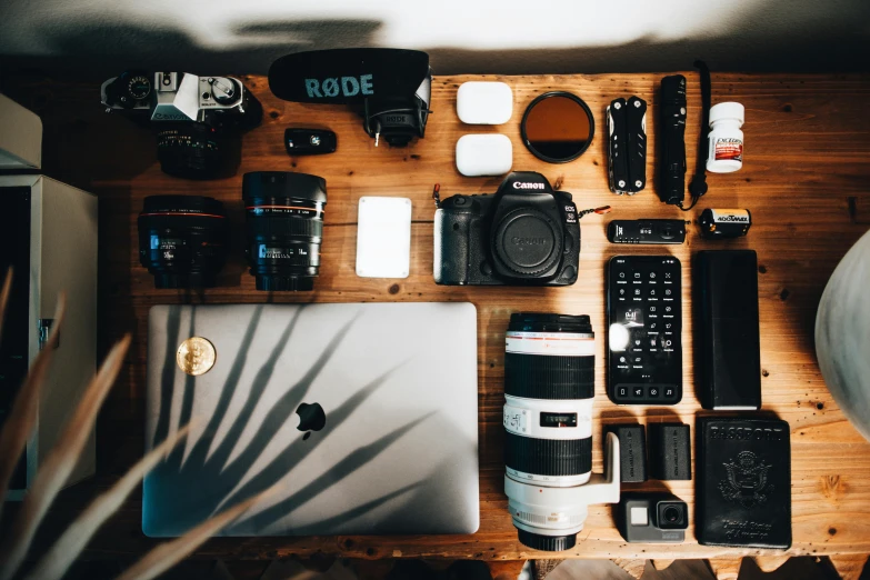 an open laptop computer sitting on top of a wooden table, a picture, by Robbie Trevino, trending on pexels, art photography, holding a big camera, full of things, with nikon cameras, knolling